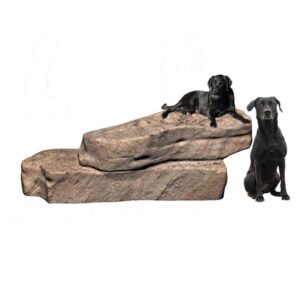 Two black dogs on large, stacked artificial rocks; one dog is lying on top, the other is sitting beside the rocks. The background is white.