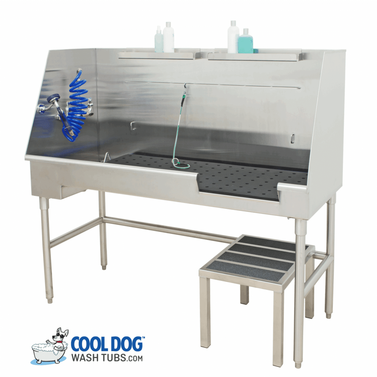Stainless steel dog wash tub with sprayer, blue hose, bottles of soap on a shelf, removable black mat, and a two-step platform. "Cool Dog Wash Tubs" logo with a cartoon dog in a bathtub appears in the corner.