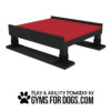 A black and red Training Platform (L/X) with sturdy legs for dog play and agility training. Text below reads "Play & Agility Powered by GymsForDogs.com" with a paw print icon.