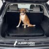 A medium-sized brown and white dog sits in the back of an SUV on a Jump Dog SUV Pet Comfort Pad, with "JUMPDOG.com" and a dog silhouette logo displayed at the bottom of the image.