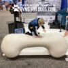 A young boy kneels on a large Agility Bone (FBR) – 4 ft Standard Weight play structure at an indoor event, surrounded by Gyms For Dogs banners featuring their innovative dog park equipment.