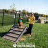 A woman and her dog enjoy the vibrant dog park while standing on the Hill Climb ramp.