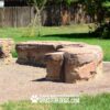 Large artificial rock structures sit on a gravel-covered area in a grassy yard, with a wooden fence and trees in the background. Text at the bottom reads, "Play & Agility Powered By GYMS FOR DOGS.COM.