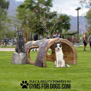 A black dog statue and a white dog with black spots sit on grass beside the Log Tunnel Climb - Interactive Play Series. People and trees are in the background. Text: "Play & Agility Powered by GymsForDogs.com.