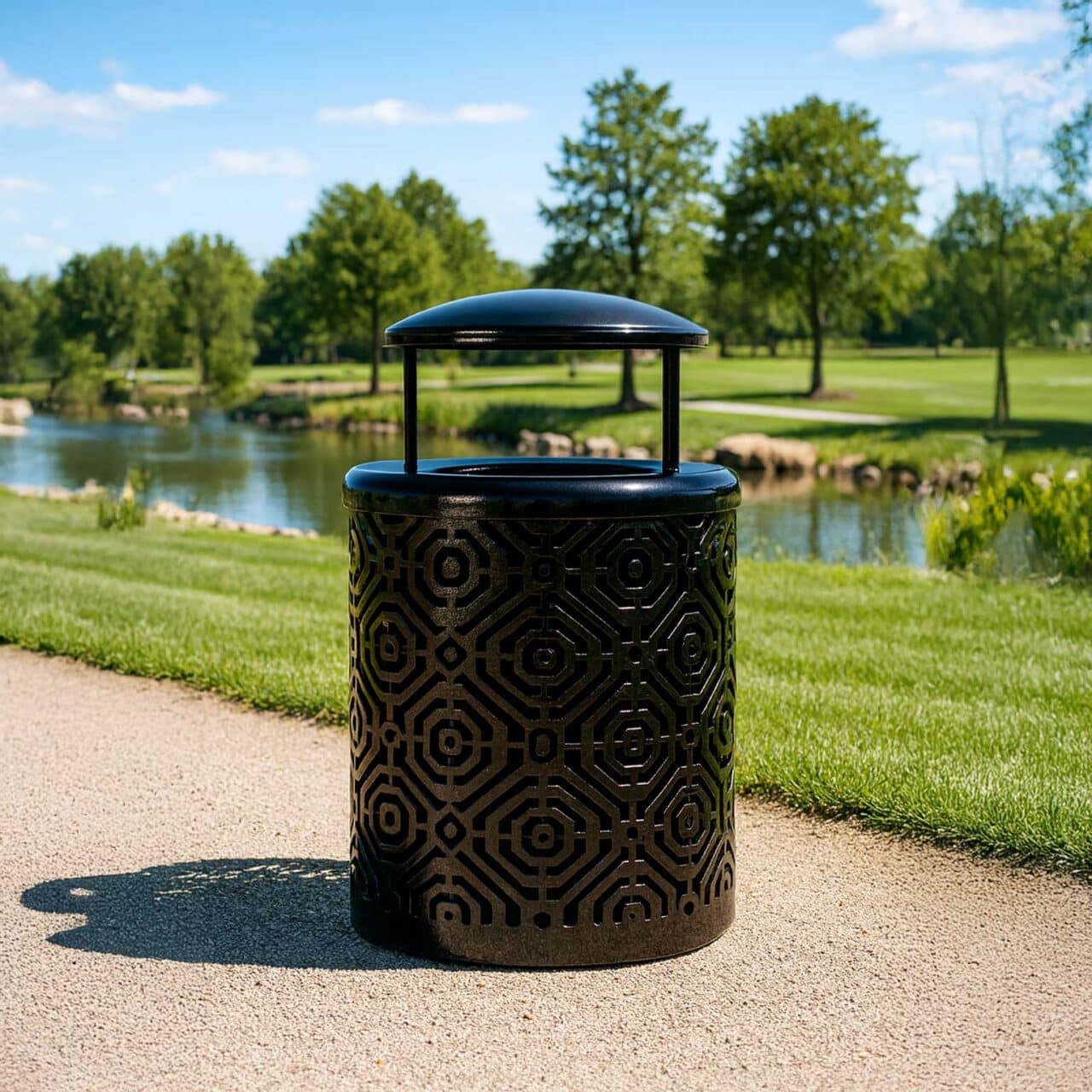 A black trash can with a bonnet lid, sunlight casting shadows on a pathway by a small pond in a green park.