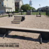 A fenced Dog Park includes the Jump Balance Beam agility equipment and benches on a gravel surface. Apartment buildings and a water tower appear in the background. Logo: "Gyms for Dogs.