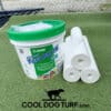 A container of Mapei Ultrabond Turf PU 1K adhesive and three rolls of white material sit on artificial grass with the COOLDOGTURF logo featuring a dog silhouette below them.