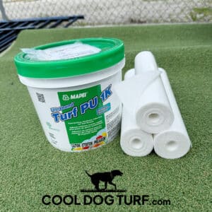 A container of Mapei Ultrabond Turf PU 1K adhesive and three rolls of white material sit on artificial grass with the COOLDOGTURF logo featuring a dog silhouette below them.