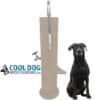 A large black dog sits beside the Doggie Demand COOL DOG Fresh Flow Water Fountain Spout and Pet Hose (SLV), a tall, beige outdoor unit with spout, faucet, and bowl. The "Cool Dog" logo with a dog's head is shown on the left side.