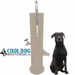 A large black dog sits beside the Doggie Demand COOL DOG Fresh Flow Water Fountain Spout and Pet Hose (SLV), a tall, beige outdoor unit with spout, faucet, and bowl. The "Cool Dog" logo with a dog's head is shown on the left side.